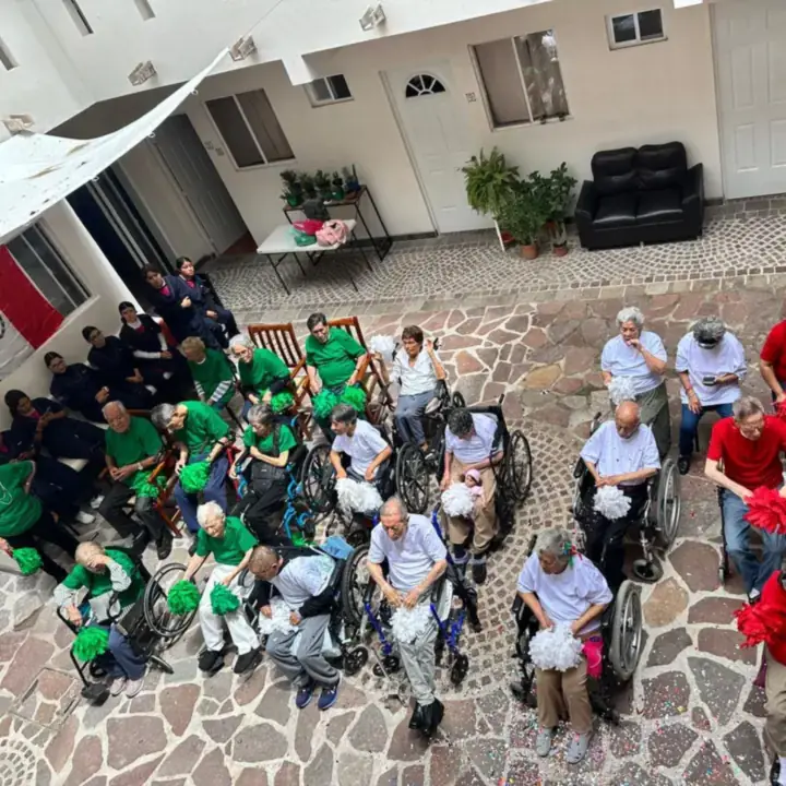 Residentes de Villas Legado Senior Living celebrando las fiestas patrias con pompones verdes, blancos y rojos en el patio de la residencia